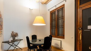 A dining area with a round table, four chairs, a hanging lamp, a window with wooden frames, and a radiator. - Deluxe two bedrooms apartment (Barcelona)