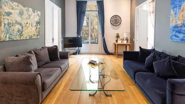 A living room with two sofas, a glass coffee table, a TV, and a window with curtains. - Deluxe two bedrooms apartment (Barcelona)