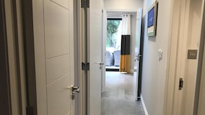 Un couloir avec des portes blanches, un luminaire au plafond et une vue sur une pièce dotée d’une fenêtre et de rideaux.