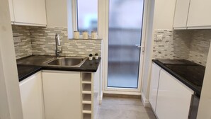 Une cuisine compacte avec des meubles blancs, un plan de travail noir, un évier en acier inoxydable et une porte en verre dépoli.