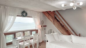 Una stanza con un divano bianco, un tavolo da pranzo con sedie, una lampada e vista sul mare.
