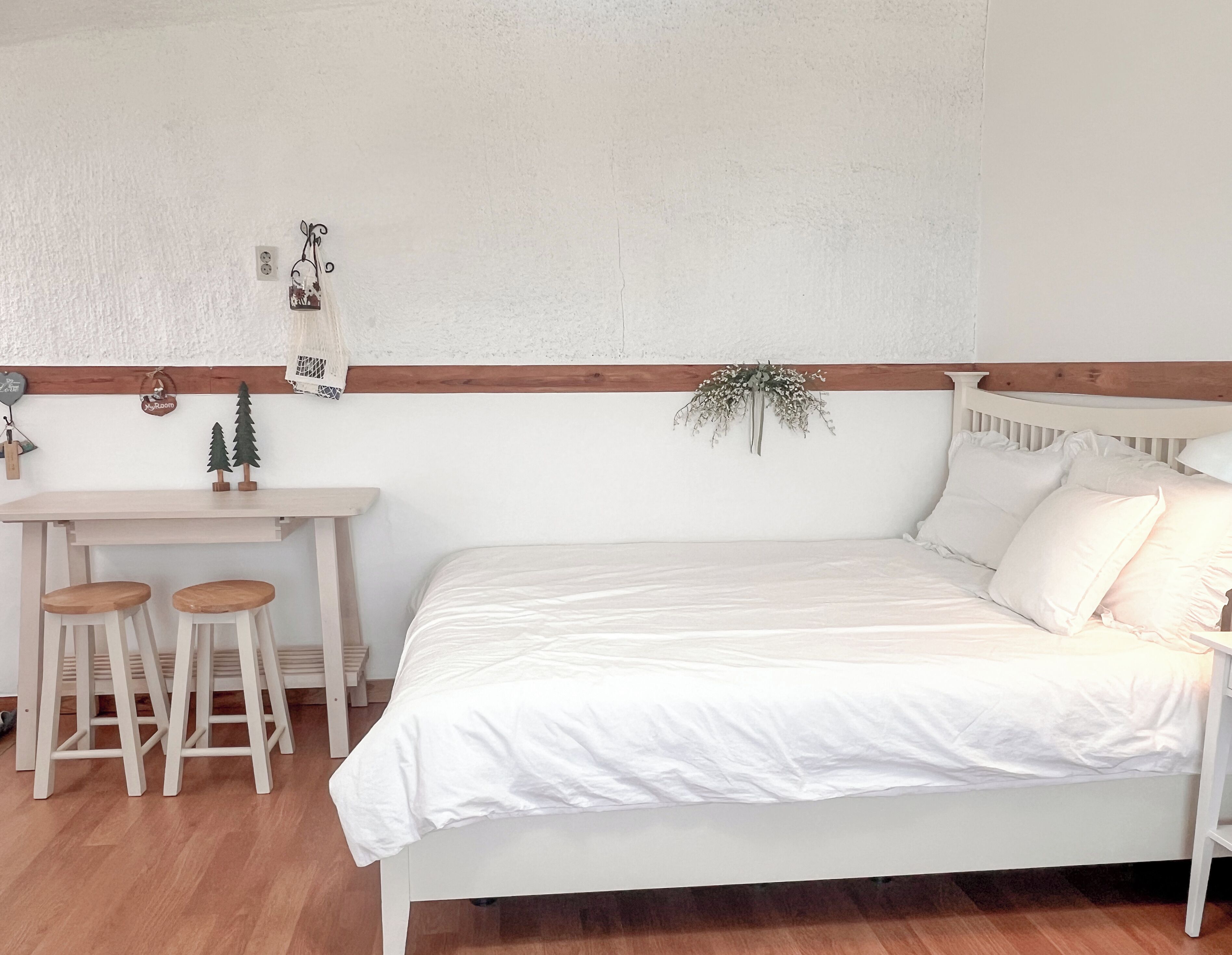 Un dormitorio con cama, un escritorio pequeño con taburetes y un estante de pared con adornos.
