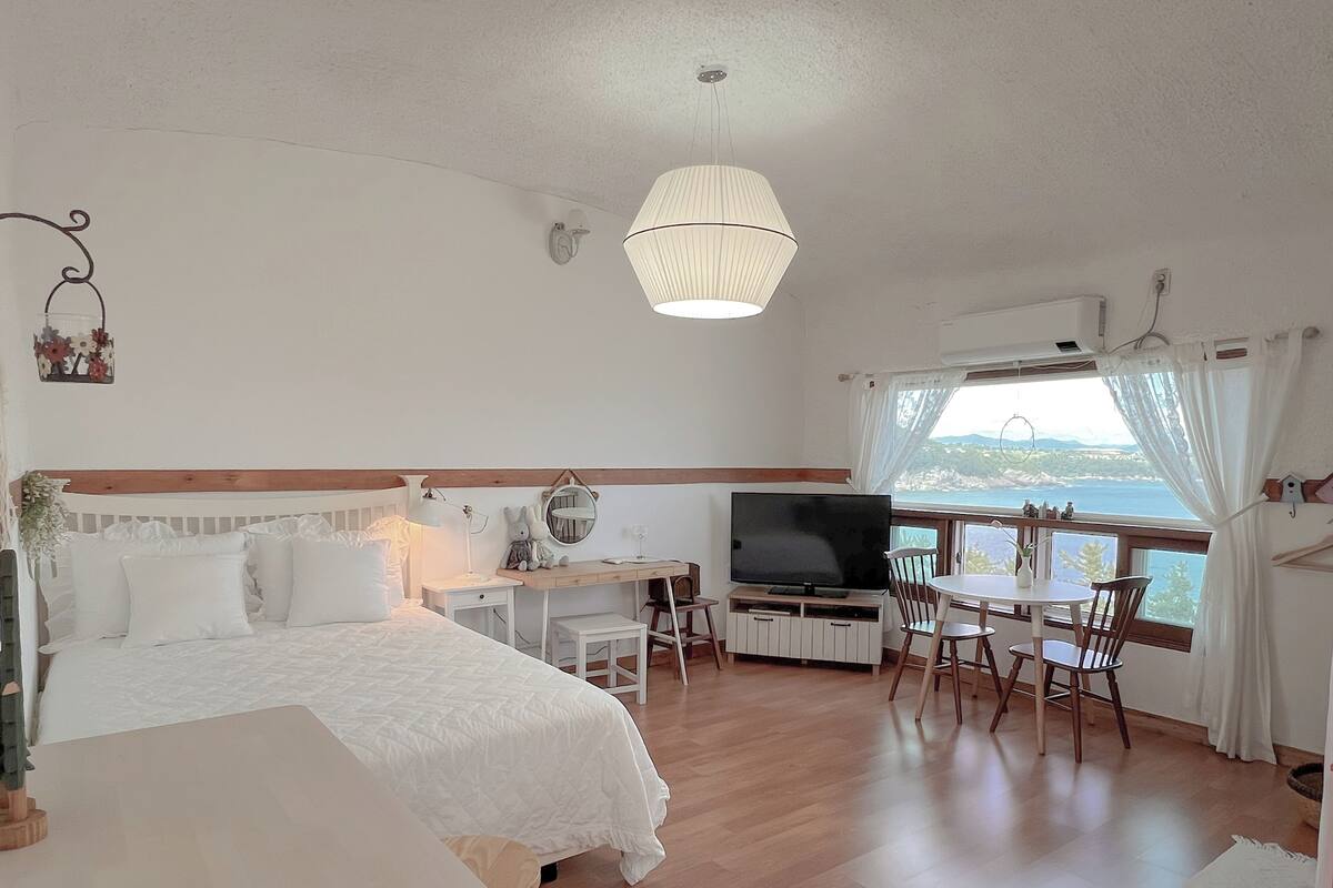 Un dormitorio con cama, escritorio, televisor y vista al mar.