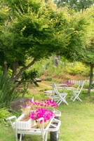 Un jardín con mesa y sillas de picnic, rodeado de abundante follaje y plantas con flores.