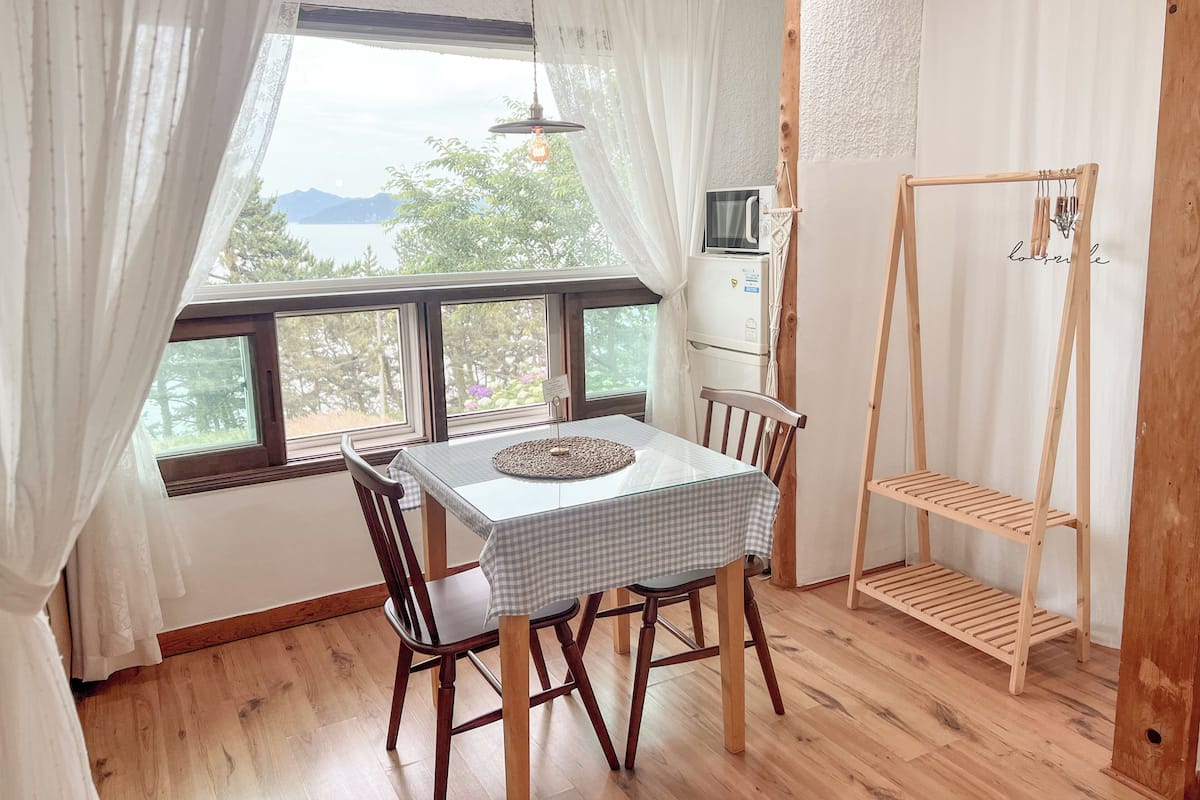 Un comedor con mesa y sillas, una estantería de madera y vistas al exterior a través de amplios ventanales.
