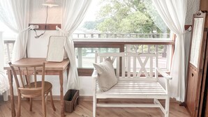 Una stanza accogliente con una scrivania in legno, una panca bianca e vista su un balcone con ringhiera.