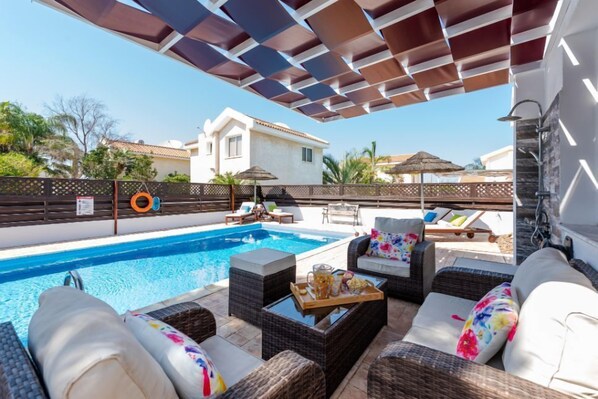 Uma área na piscina com móveis de vime, piscina e um espaço coberto para sentar.