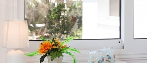Una mesita de noche blanca con una lámpara, un florero con flores naranjas y dos frascos decorativos.