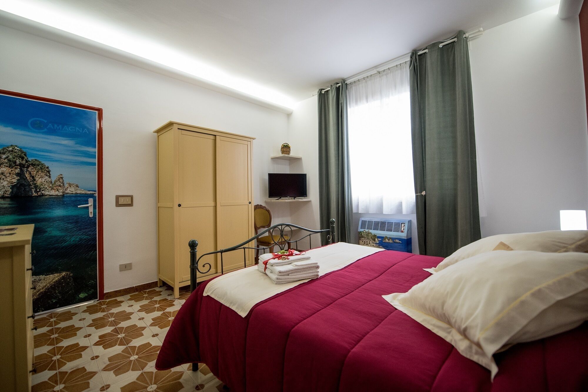 A bedroom with a bed, a wardrobe, a television, and a window with curtains.