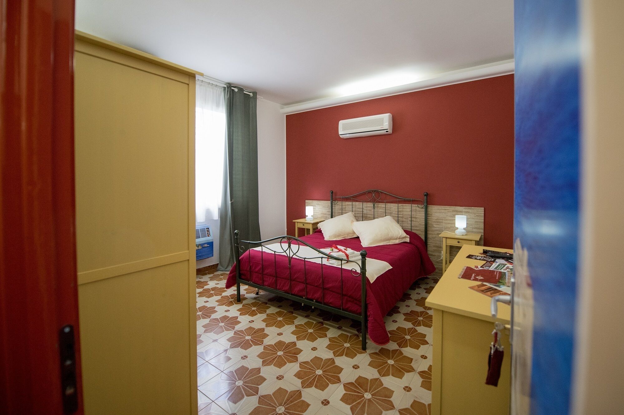 Habitación de hotel con cama, mesitas de noche, unidad de aire acondicionado y suelo estampado.