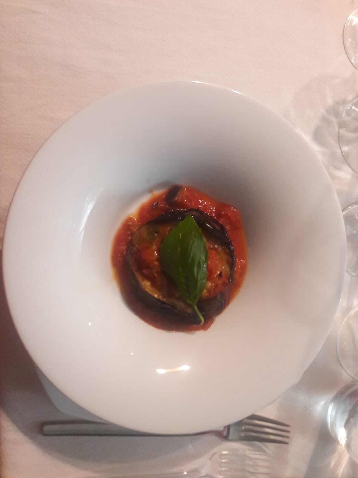 A white plate with a dish of stuffed eggplant in tomato sauce, garnished with a basil leaf, on a table.