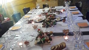 Una mesa de comedor dispuesta con platos, cubiertos, vasos y un centro de mesa con comida y flores.