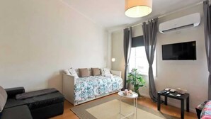 A modern living room with a sofa, a small table, a TV, and an air conditioning unit.