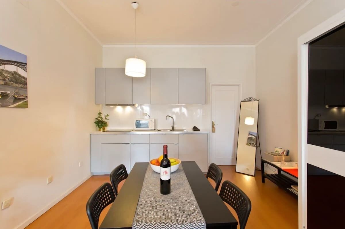 Una cocina moderna con armarios grises, una mesa de comedor con una botella de vino y un espejo grande.