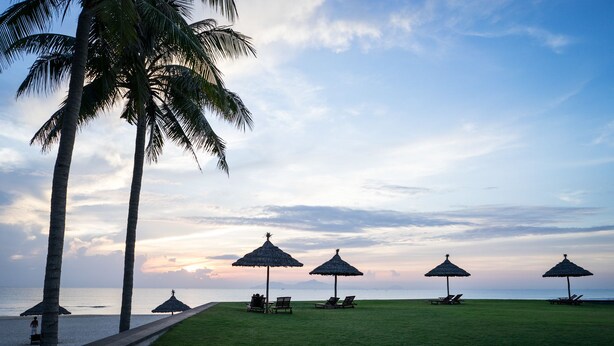 A beach with palm trees, thatched umbrellas, and lounge chairs. - The Ocean Suites - A504 Tower A (Da Nang)