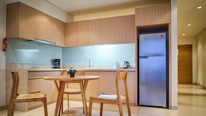 A modern kitchen with wooden cabinets, a stainless steel refrigerator, a coffee maker, and a dining table with chairs. - The Ocean Suites - A504 Tower A (Da Nang)
