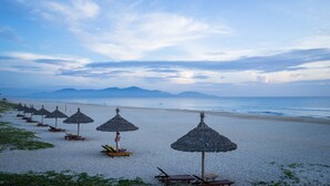 A beach with rows of thatched umbrellas and lounge chairs. - The Ocean Suites - A504 Tower A (Da Nang)