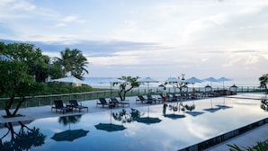 A poolside area with lounge chairs and umbrellas, overlooking a beach with palm trees and a clear sky. - The Ocean Suites - A504 Tower A (Da Nang)