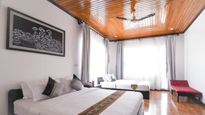 Habitación de hotel con dos camas, un ventilador de techo, un cuadro en la pared y vistas al exterior a través de amplias ventanas.