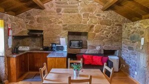 Une cuisine rustique aux murs de pierre, aux poutres apparentes et agrémentée d’un lustre.
