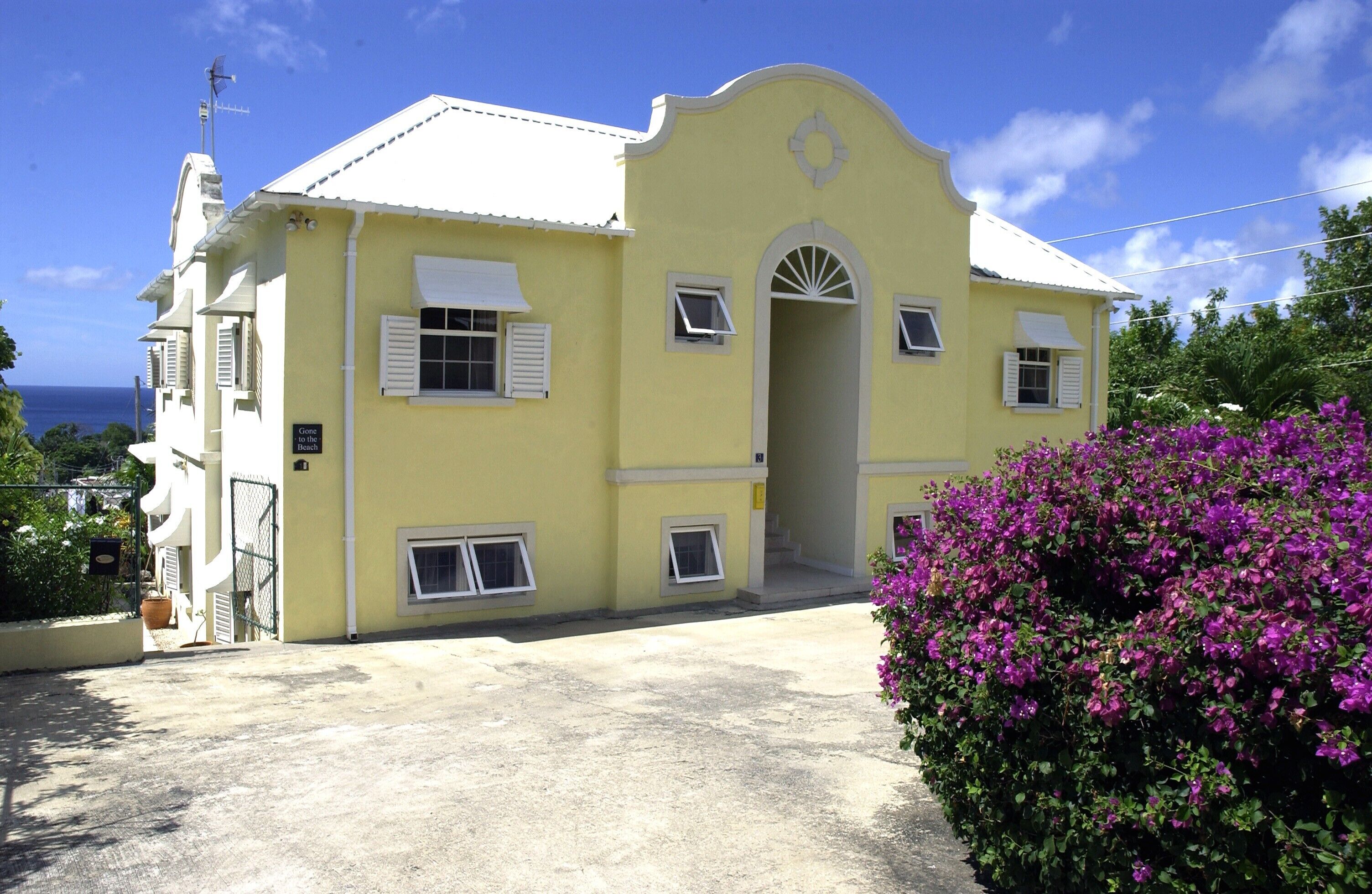 A yellow building with a white door and windows, a sign that reads "Close to the Beach," and a purple flower bush in the foreground.