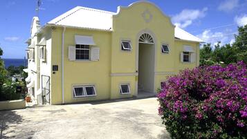 A yellow building with a white door and windows, a sign that reads "Close to the Beach," and a purple flower bush in the foreground.
