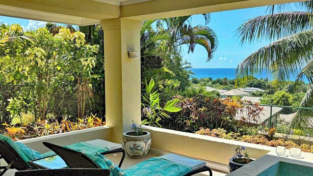 Un balcón con piscina, sillones de descanso y vistas al océano y la vegetación tropical.