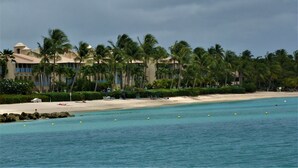 Un hotel frente al mar con playa, palmeras y aguas cristalinas.