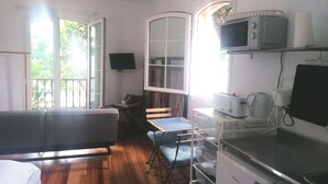 A compact kitchen with a microwave, toaster, and coffee maker. There is a dining area with a table and chairs, and a sofa. A TV is mounted on the wall. - SWEET DREAMS Beautiful Apartment. Light, Comfort, Tranquility (Sta Brígida)