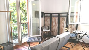 A modern living room with a sofa, a small table, and a view of greenery through large glass doors. - SWEET DREAMS Beautiful Apartment. Light, Comfort, Tranquility (Sta Brígida)