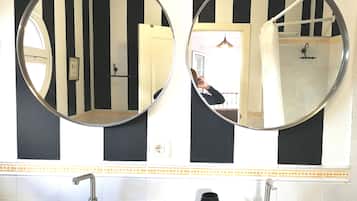 Dos espejos redondos colocados en una pared con azulejos a rayas negras y blancas, un lavamanos blanco con un jabonera negra, y un perchero con una toalla.