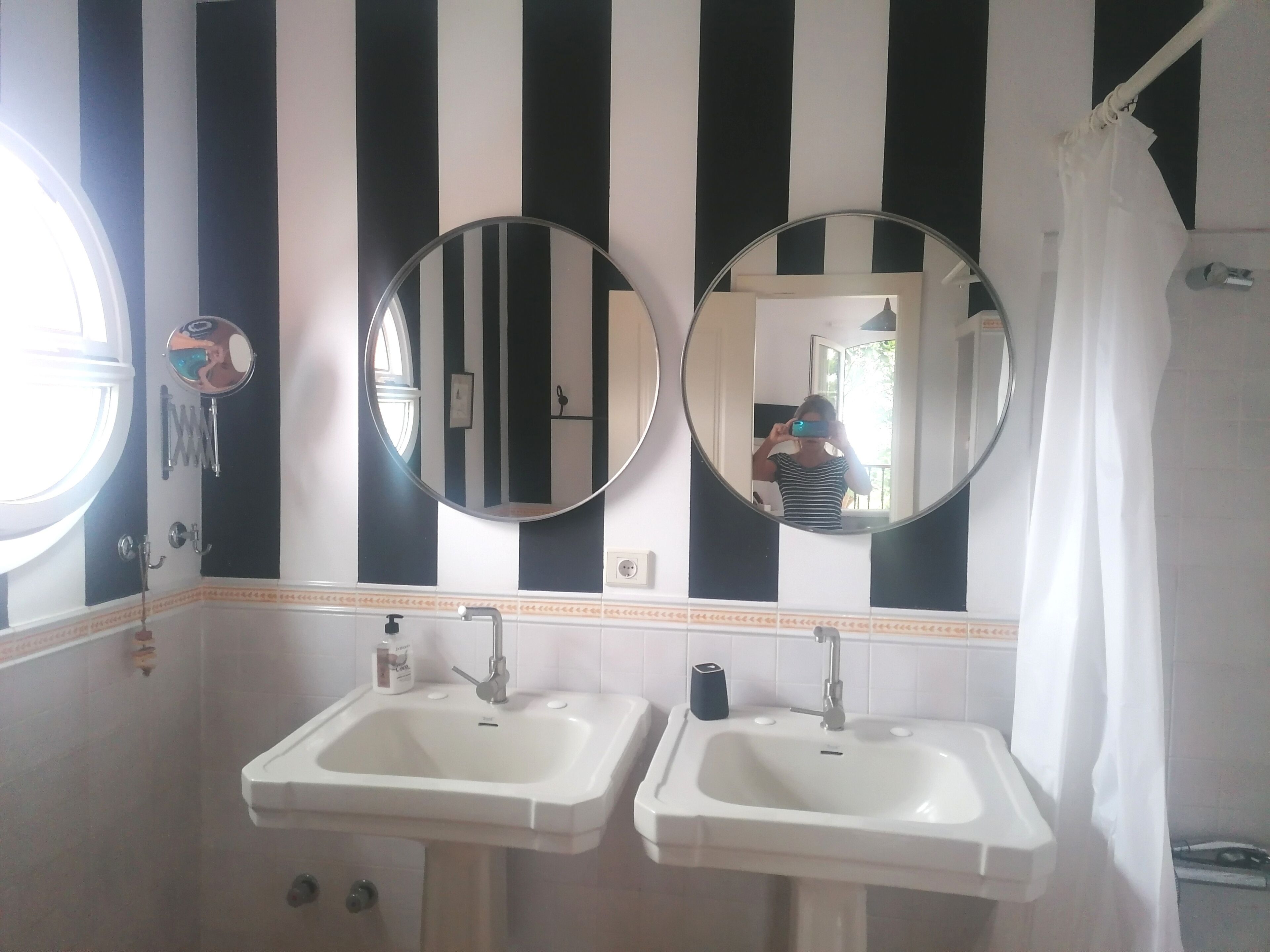 Un baño con dos lavamanos, un espejo y una pared a rayas.