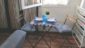 A compact dining area with a table set for two, a small potted plant, and a view of a hilly landscape through a window. - SWEET DREAMS Beautiful Apartment. Light, Comfort, Tranquility (Sta Brígida)
