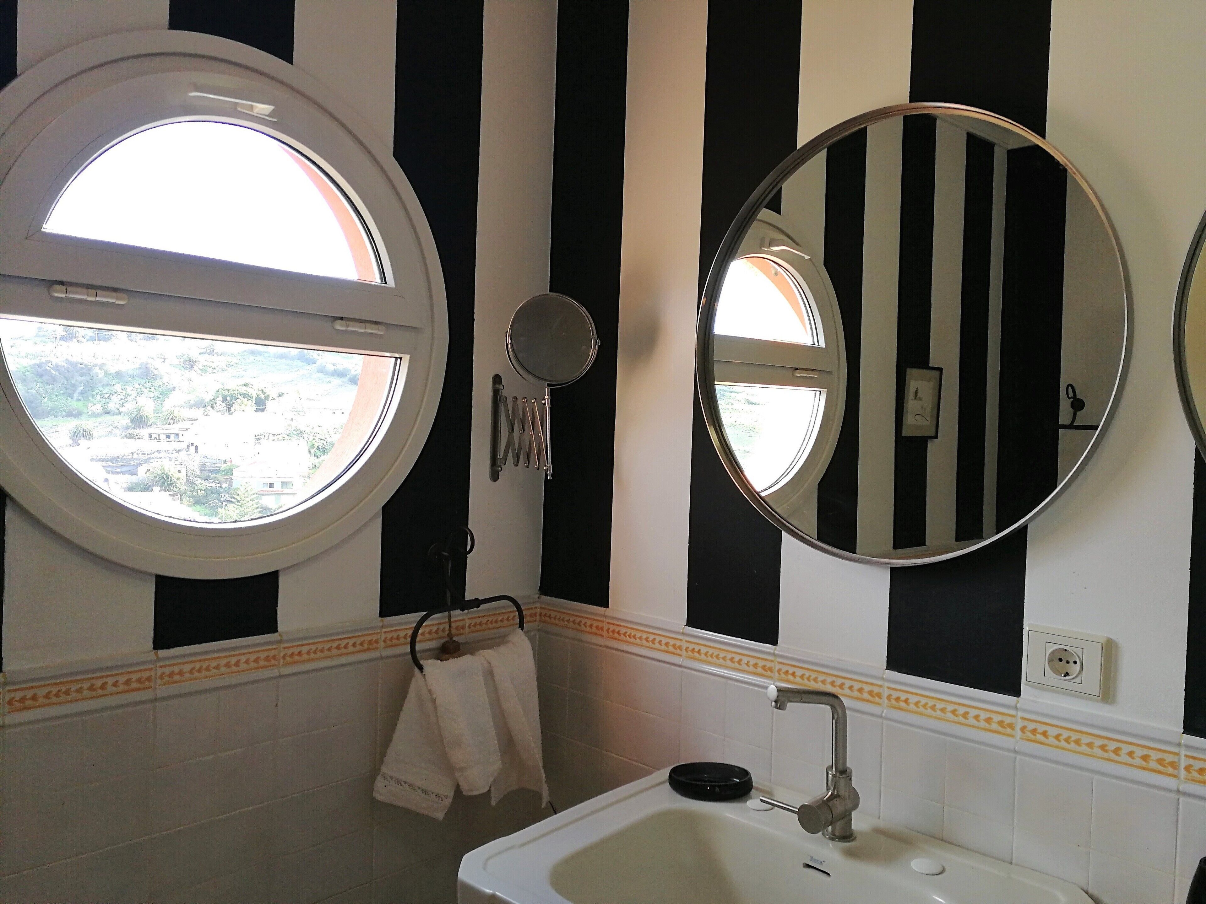 Une salle de bain avec une fenêtre ronde, un miroir rond et un lavabo.