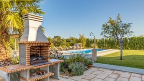 Une terrasse extérieure avec un barbecue en briques, une piscine et des chaises longues.