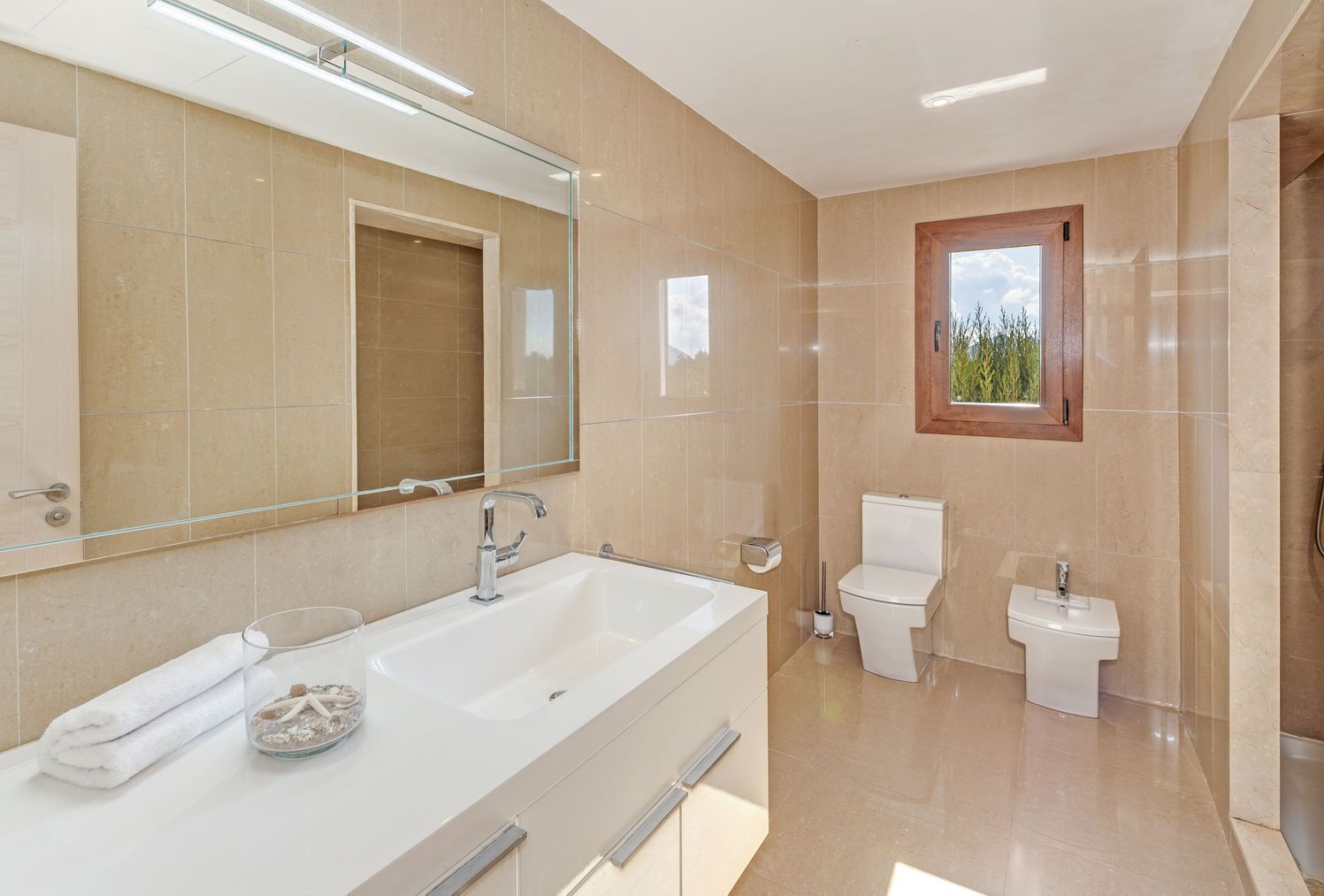 Un baño moderno con un espejo grande, lavamanos doble, inodoro y bidé.