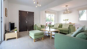Ein modernes Wohnzimmer mit grünen Sofas, einem Couchtisch und einem Fernseher auf einem Schrank.