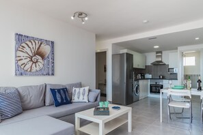 A modern living room with a grey sofa, a white coffee table, and a kitchen in the background.