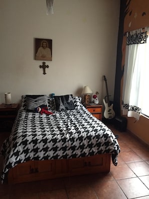 A bedroom with a bed, a cross on the wall, a guitar, and a lamp.