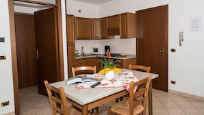 Un coin repas avec une table dressée pour deux personnes, des chaises en bois, un livre, un vase avec des fleurs et un four à micro-ondes en arrière-plan.