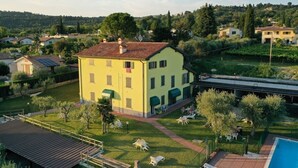 Un bâtiment jaune avec un toit rouge, entouré d’une piscine, d’un jardin et d’un pont.