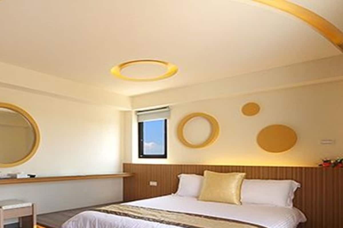 A hotel room with a bed, a bedside table, a mirror, and a window.