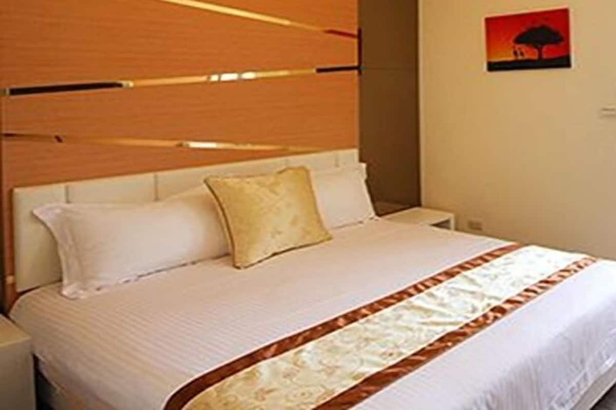 A hotel room with a bed, a wooden headboard, an air conditioning unit, and a wall-mounted artwork.