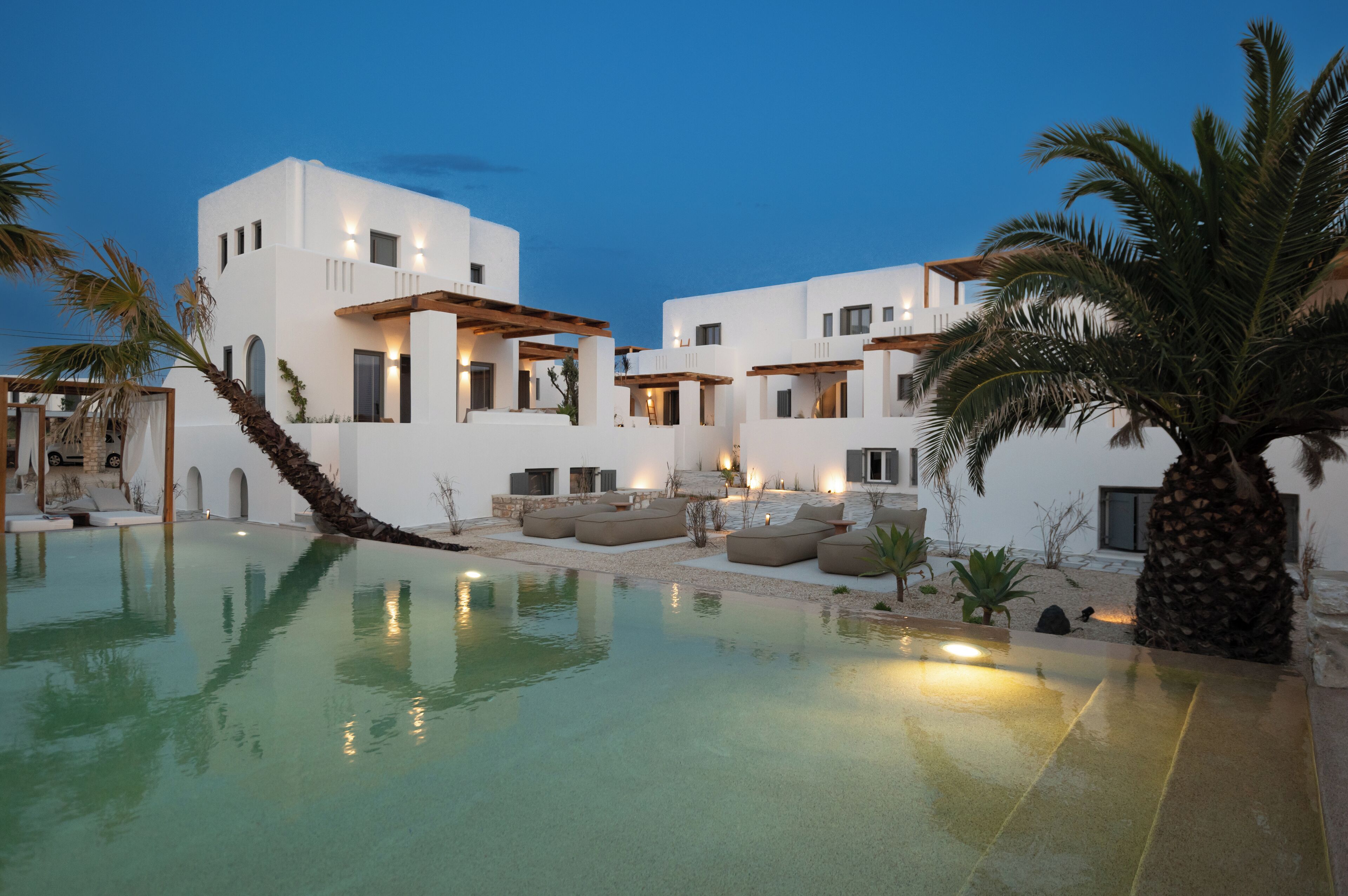 A modern resort with a swimming pool, outdoor seating, and a palm tree.