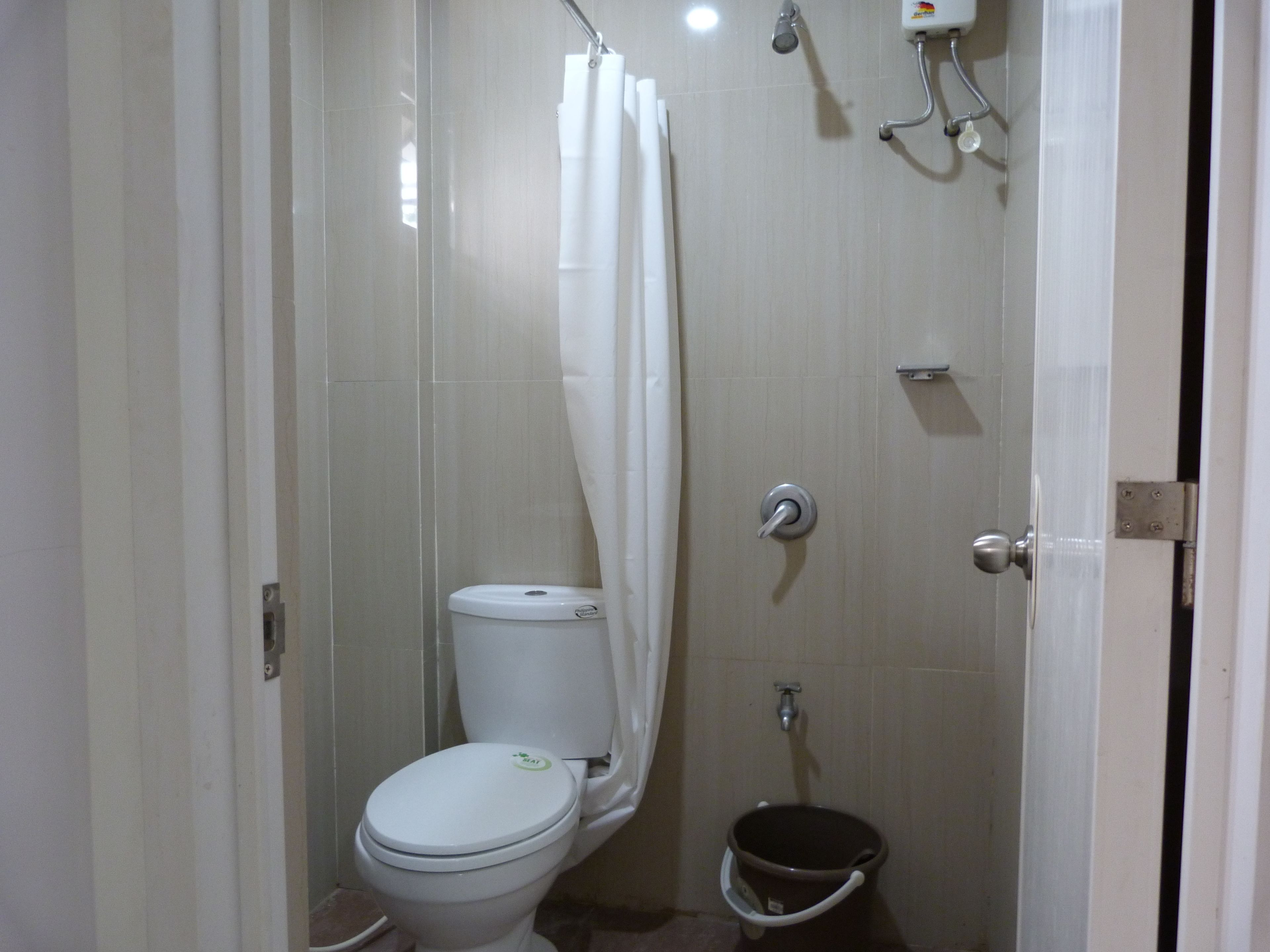 Un baño pequeño y cerrado con inodoro, ducha y un balde.
