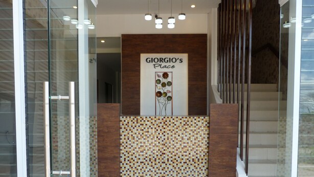 A modern interior with a tiled mosaic wall, a wooden reception desk, and a staircase. - Giorgio's Place (Polomolok)