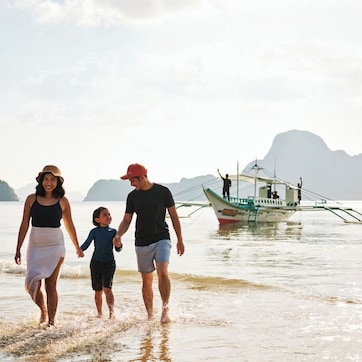 A family walking on a beach with a boat in the background.