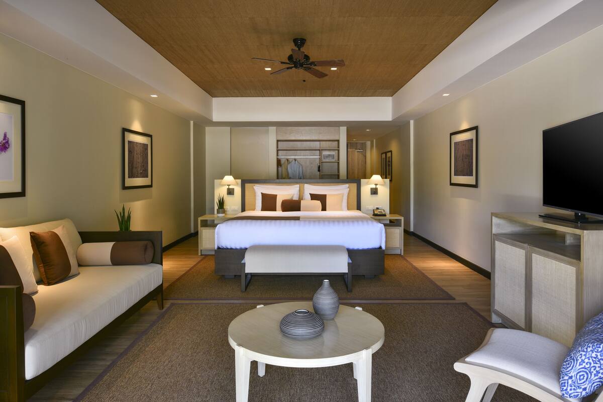A modern hotel room with a bed, a sofa, a TV, and a small table.