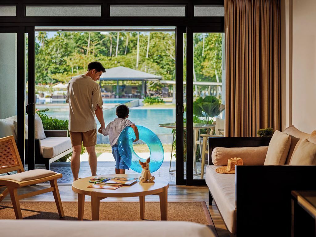 Une pièce dotée d’une grande porte vitrée donnant sur un espace piscine, d’un canapé, d’une table basse et d’un petit chien.