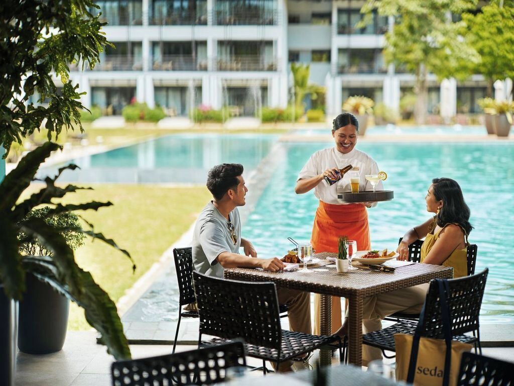 A dining table with chairs, a waiter, and a poolside setting with a building in the background.